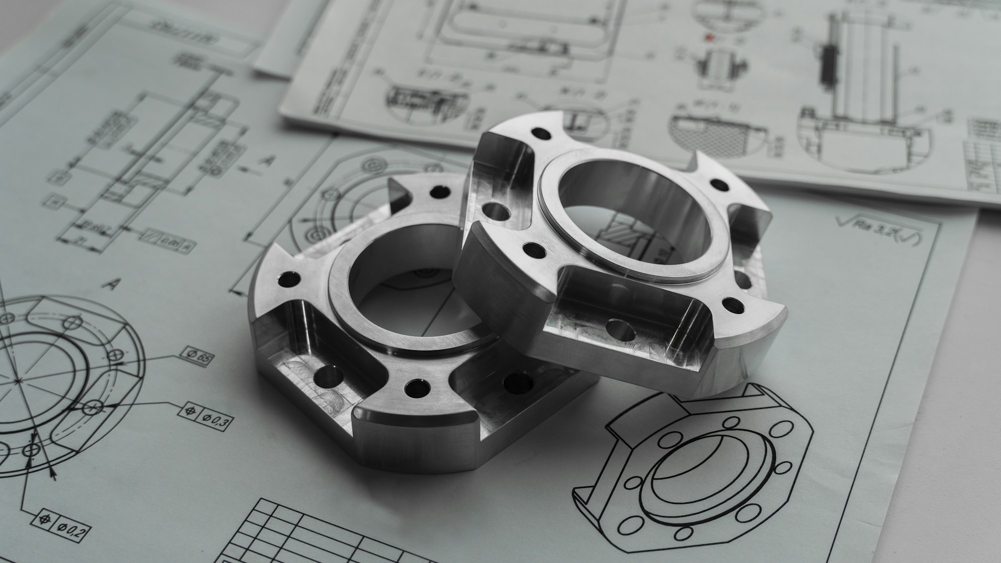 Two machined metal parts resting on engineering drawings