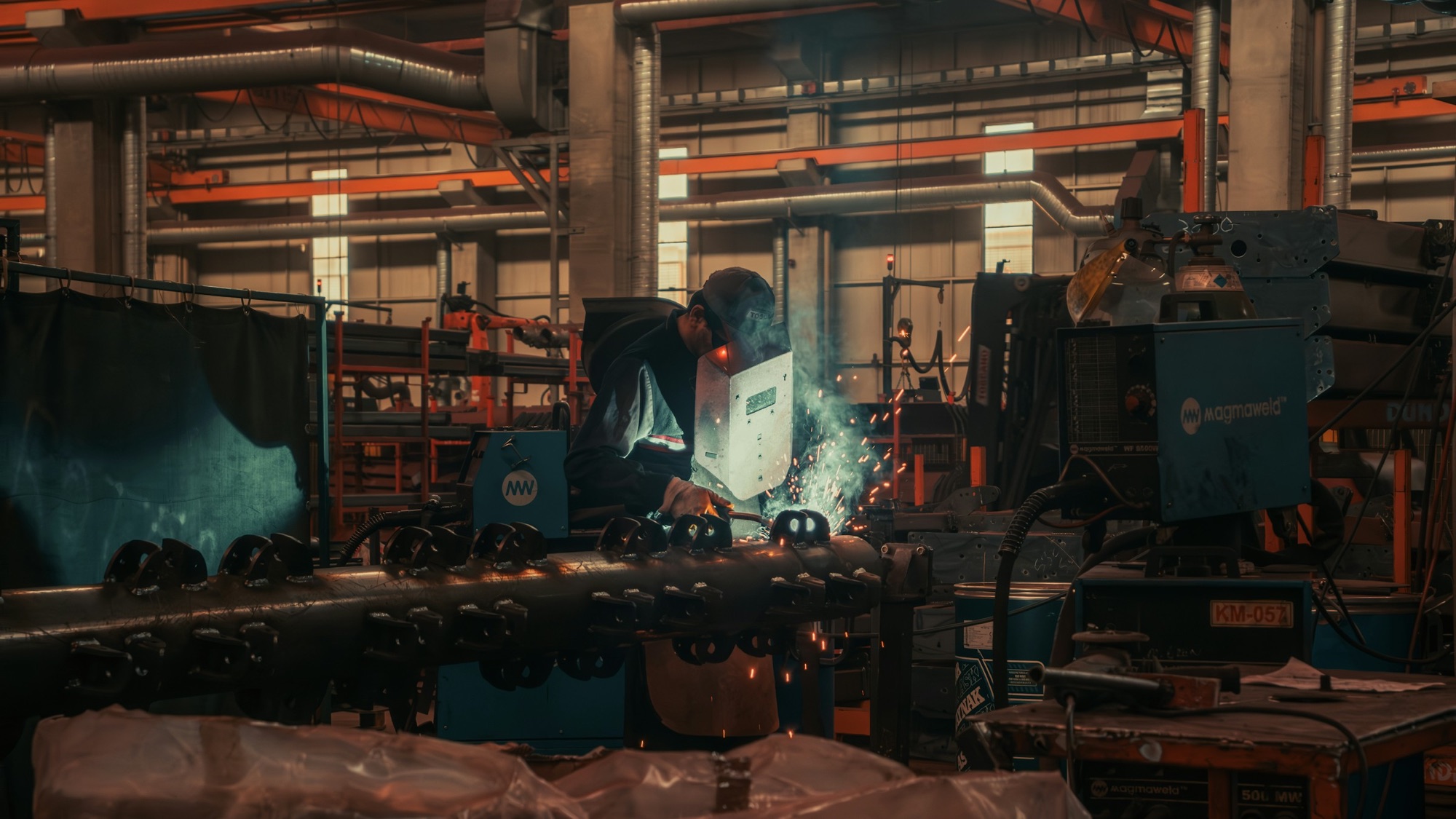 A welder at work on a factory floor, sparks lighting the bench
