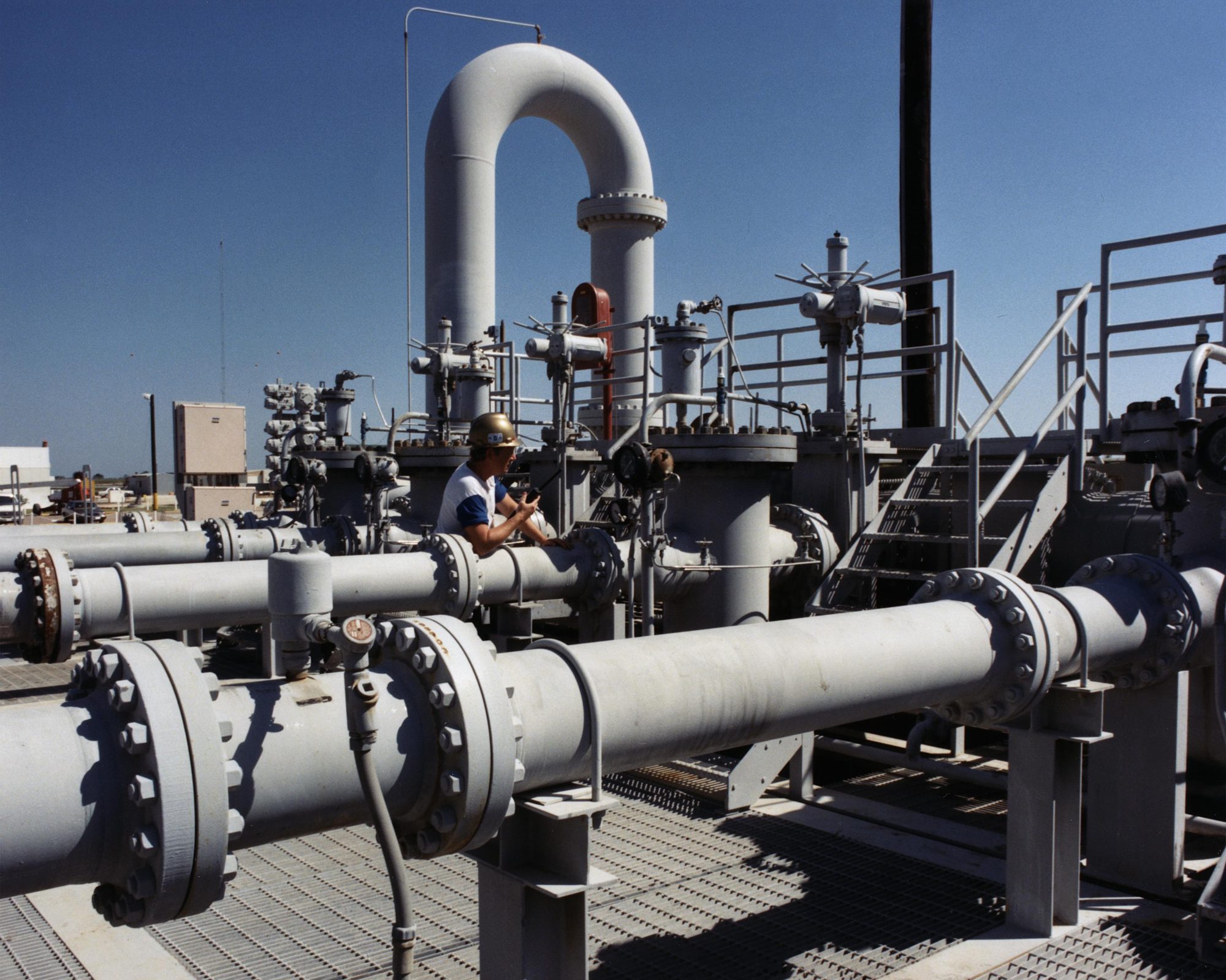 A technician working on flanged process piping beside a vessel at a crude oil facility